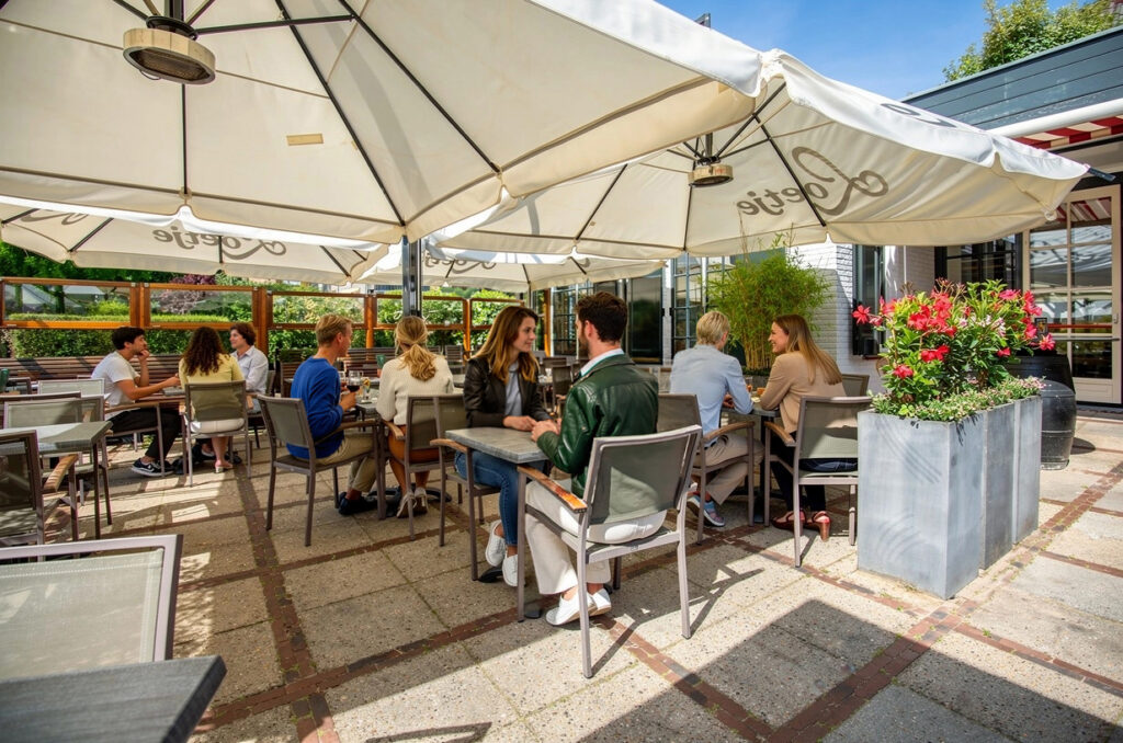 Gasten op het zonnige terras van Loetje aan de Amstel onder grote parasols.