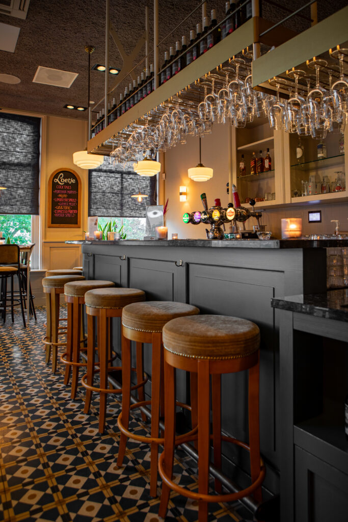 De bar van Loetje Leeuwarden met houten barkrukken, hangende wijnglazen en warme verlichting.