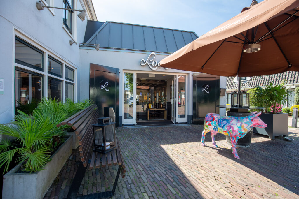 Entree van Loetje aan de Amstel met terras, parasol en de kleurrijke Loetje-koe.